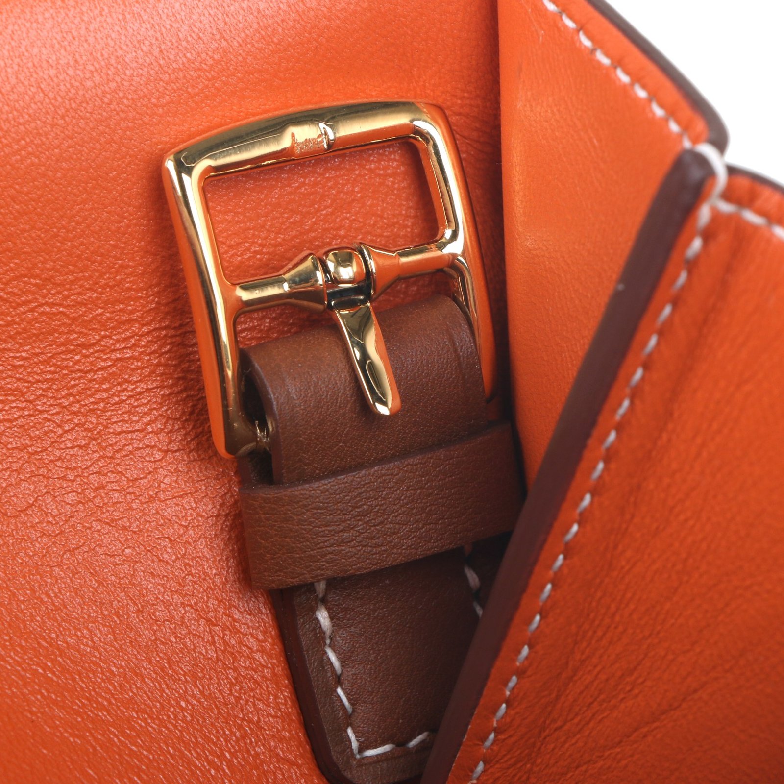 Close-up of an orange and brown leather handbag with gold-tone clasp hardware and white stitching